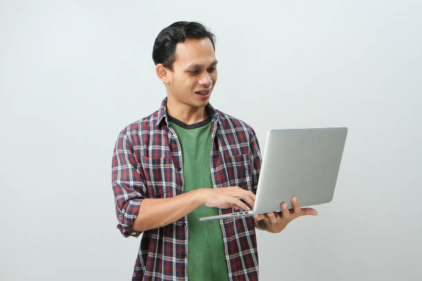 istock Happy asian indonesian man holding laptop computer on isolated background 1997255082