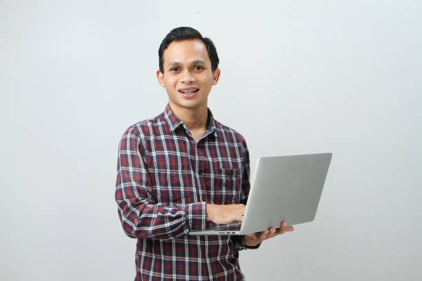 istock Happy asian indonesian man holding laptop computer on isolated background 1997255088