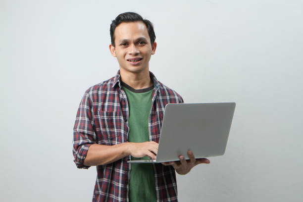 istock Happy asian indonesian man holding laptop computer on isolated background 1997256677