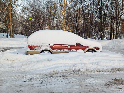 A car covered in snow in a parking lot. Snowdrifts in the city after a snowfall.
