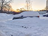 A snow-covered car in a parking lot against the background of the dawn sky.