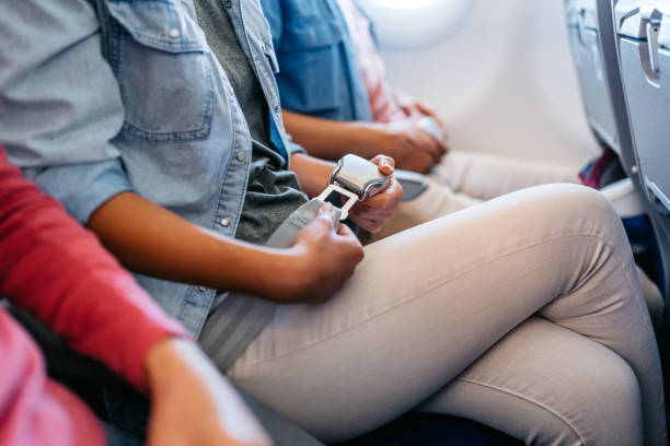mujer joven abrochándose el cinturón de seguridad en un avión - silla al lado de la ventana fotografías e imágenes de stock