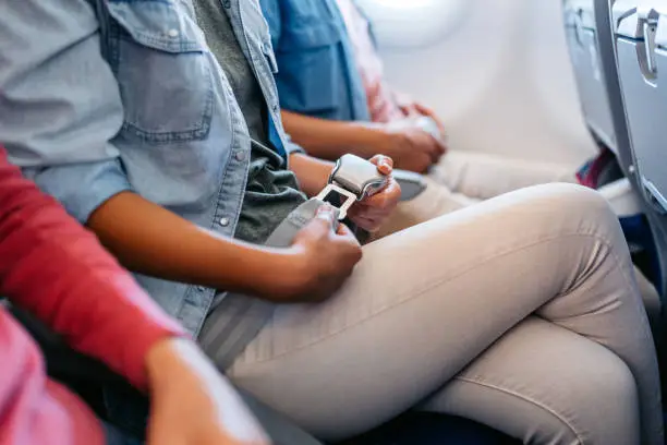 Close-up of a young woman fastening her seatbelt in an airplane.