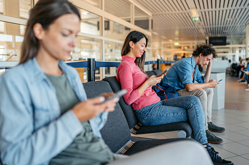 Three young people using their smart phones while waiting at the airport in Malmo, Sweden.