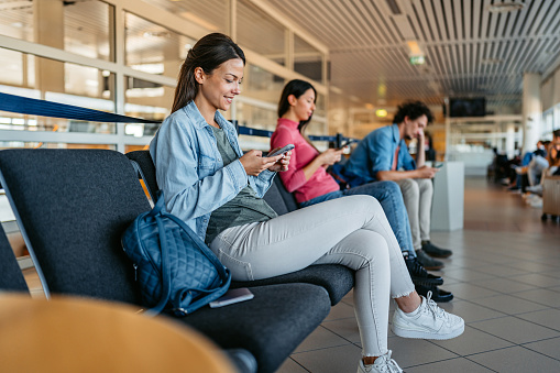 Three young people using their smart phones while waiting at the airport in Malmo, Sweden.