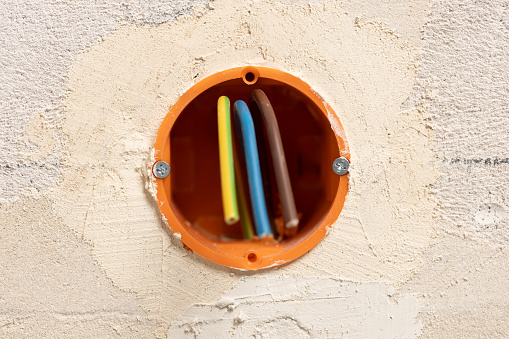 Colorful electric cables sticking out of an orange box placed in the wall