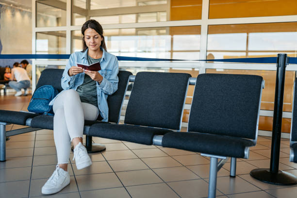 junge frau schaut auf ihren reisepass, während sie am flughafen wartet - passport sweden customs europe stock-fotos und bilder