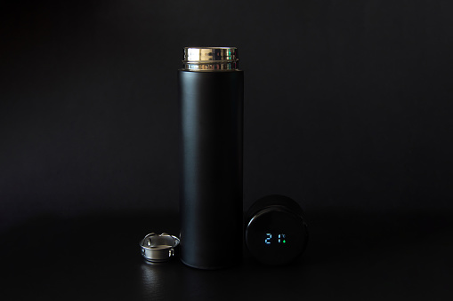 Black thermos with a strainer and a thermometer in the lid on a black background.