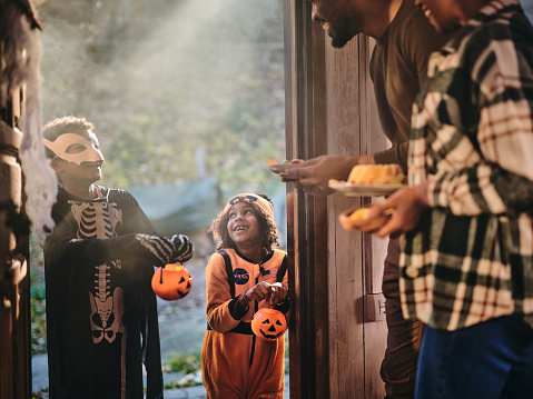 Happy African American kids in costumes came to a trick or treat at the door during Halloween celebration.