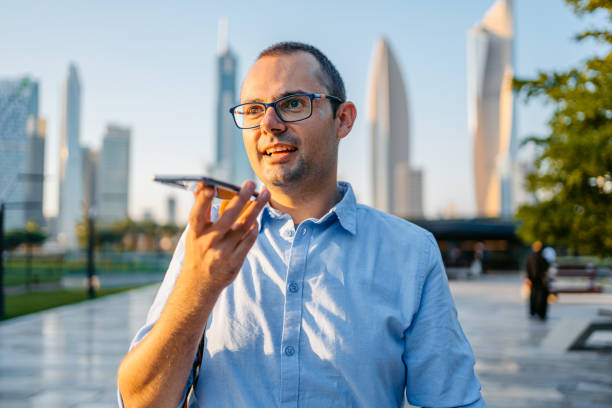 young man sending a voice message while walking in the al shaheed park in kuwait city - vocoder imagens e fotografias de stock