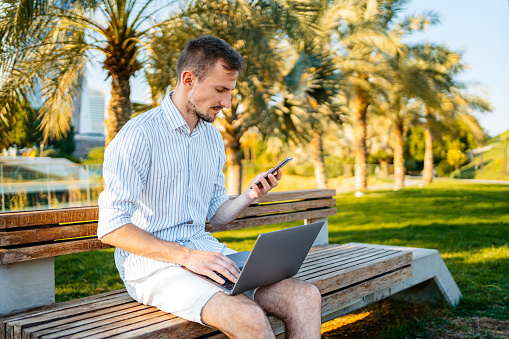 Young man using phone and a laptop in the Al Shaheed park in Kuwait City In Kuwait.