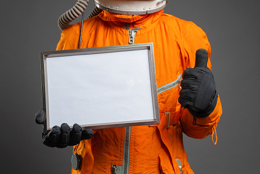 Astronaut holding in hand a blank diploma certificate with copy space. Space message. Space program goals template.