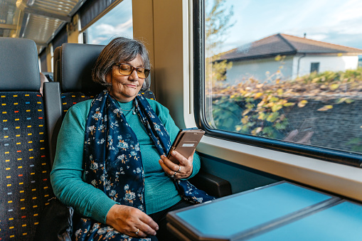 Beautiful senior woman using her smart phone while riding in a train in Switzerland.