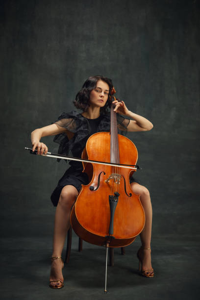 istock Cellist's debut, classical album. Elegant young woman making solo performance, playing cello against dark vintage green background. 1997432523