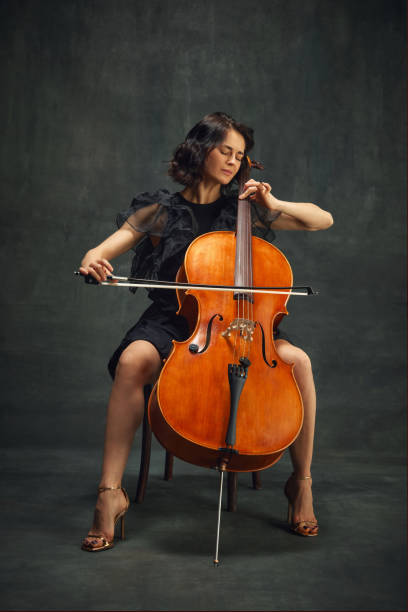 istock Cellist, elegant woman in deep concentration, playing cello passionately with eyes closed against vintage green background. 1997433075