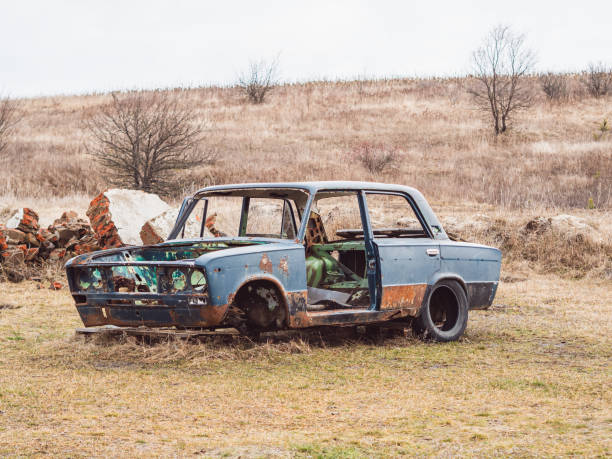 Old damaged rusty blue car on a field with dry grass.