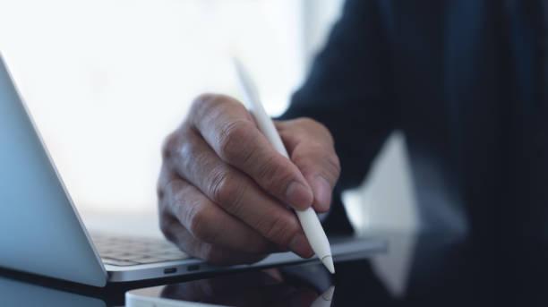 istock Businessman, manager working, using stylus pen signing e-document on digital tablet with laptop computer on table at modern office, e-signing, electronic signature, work planning, digital document concept 1997447861