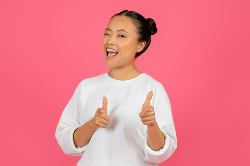 Cheerful Young Asian Woman Pointing At Camera With Two Hands And Smiling, Positive Korean Female Indicating Somebody, Saying Gotcha, Standing Isolated Over Pink Studio Background, Copy Space