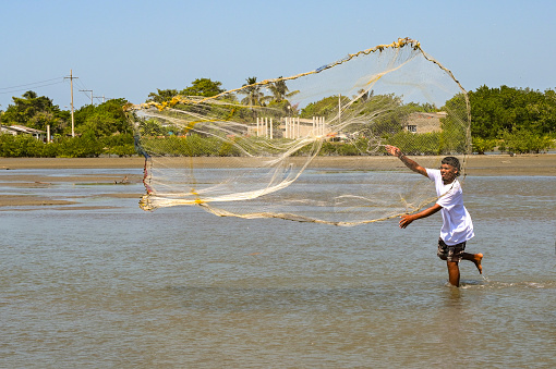 Cartagena, Colombia - 24 January 2024: Young man using a traditional fishing net on the lagoon in a village in La Boquilla on the outskirts of Cartagena.