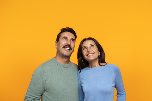 Happy funny senior caucasian family in casual look up at empty space, isolated on orange studio background. Surprise, relationships and idea, attention sale, ad and offer