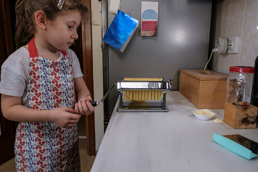 Cute Girls Preparing Pasta in Domestic Kitchen. Fresh pasta and pasta machine on the kitchen counter while rolling out dough. Preparing home made pasta with pasta maker.
