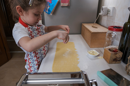 Cute Girls Preparing Pasta in Domestic Kitchen. Fresh pasta and pasta machine on the kitchen counter while rolling out dough. Preparing home made pasta with pasta maker.