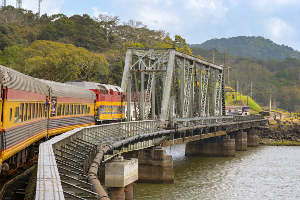 Panama - 22 January 2024: Diesel locomotive pulling coaches rounding a bend to cross a river bridge on the Panama Canal Railway