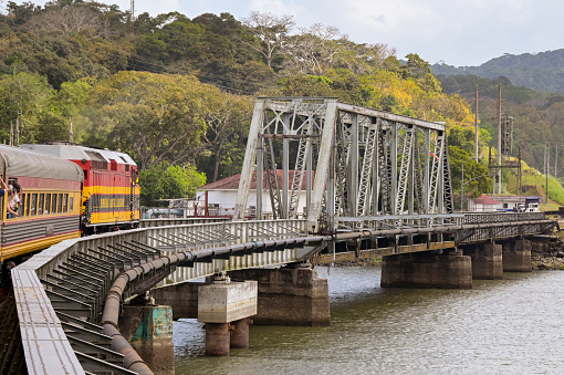 Panama - 22 January 2024: Diesel locomotive pulling coaches rounding a bend to cross a river bridge on the Panama Canal Railway