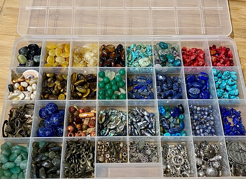 Horizontal looking down plastic organiser container with a variety of crystal beads, stones, and silver used for making hand crafted jewelery