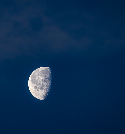The moon in a blue sky, surrounded by dark clouds