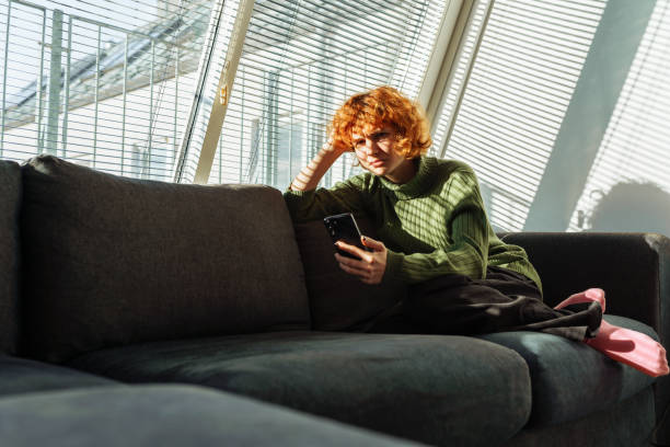 istock young red-haired woman in living room on sofa using phone 1997531064