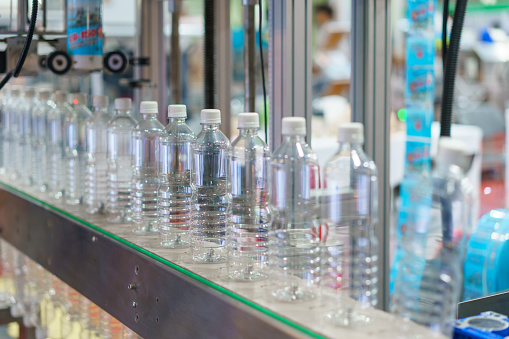 Image showcasing a row of clear plastic water bottles on a conveyor belt in a bottling plant, with focus on the bottles and the industrial machinery in the background