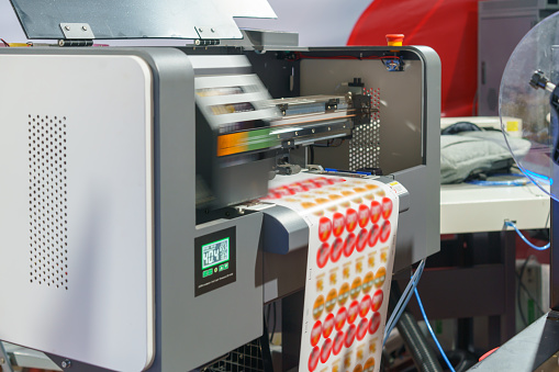 High-resolution image depicting the industrial printing process of adhesive labels, showcasing the machinery and label sheet emerging with vibrant red and orange circular designs