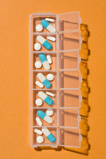 Weekly, daily pill organizer, dispenser box on orange background