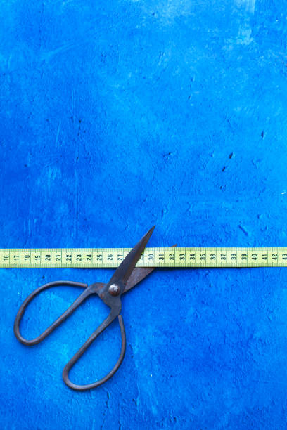 istock Scissors with large handles cutting a measuring tape on a blue background with copy space 1997622283