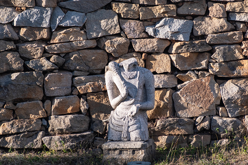 A beautifully carved stone figure is set against a rustic wall of uneven stones at the historical site of Shravanabelagola in India, bathed in the warm light of the setting sun.