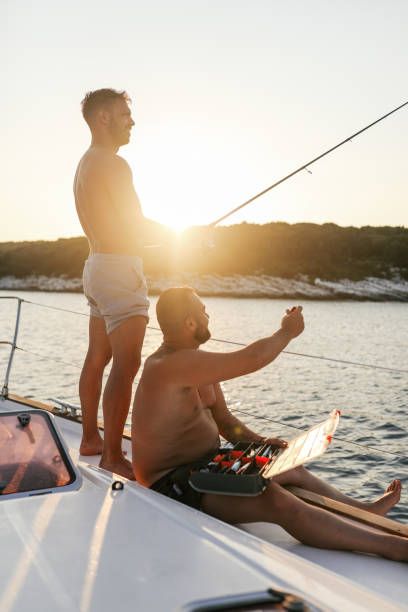 Young handsome man fishing from a sailboat deck