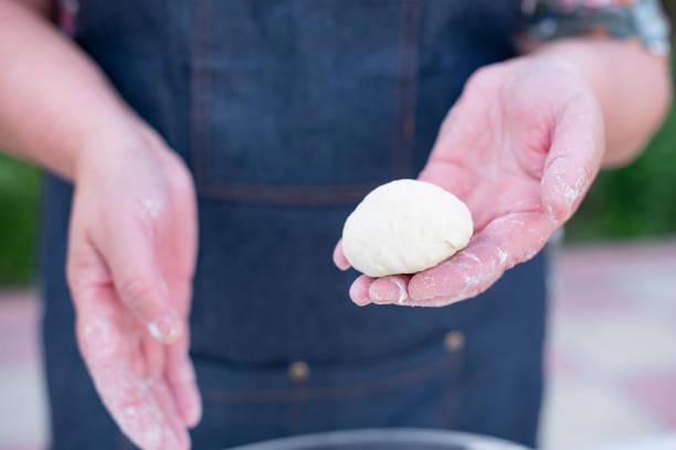 istock Old female wearing blue apron holding dough, rolling buns, showing, dusting with flour. 1997639830