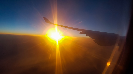 The plane is flying and the sun rises and the sunlight shines from under the wing of the Airbus 340 plane at a height