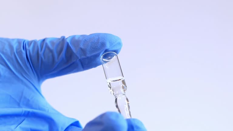 Woman's hand in a blue medical glove holds a glass ampoule