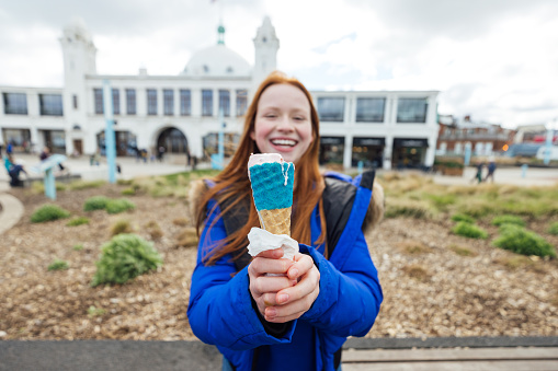 A young female teenager enjoying a weekend out in Whitley Bay, North East England. She is holding an ice cream up to the camera while looking at the camera and smiling, the focus is the ice cream while she is out of focus.
