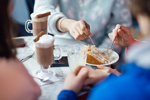 An unrecognisable group of male and female teenagers enjoying a weekend hanging out together in Whitley Bay, North East England. They are sitting in a cafe, enjoying hot chocolate refreshments and sharing a piece of cake.