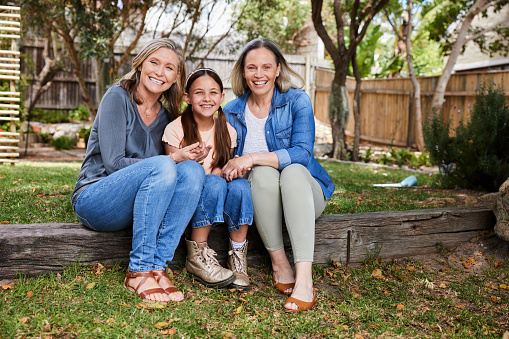 Portrait of a woman sitting with her cute little daughter and mature mother outside in a back yard at home in summer