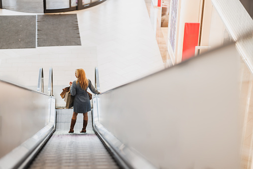 Rear view of an attractive woman carrying bags on escalator in a mall while out on a shopping spree.