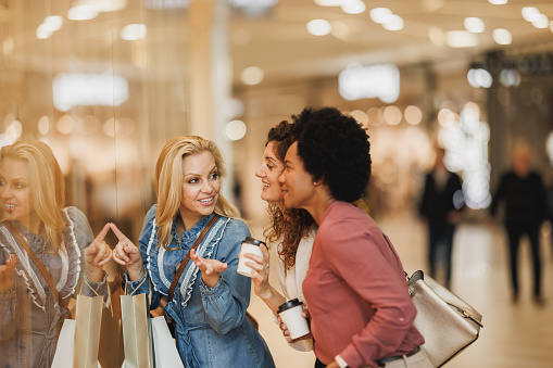 Three smiling women taking some time out to enjoy a shopping spree in the mall during Black Friday or Cyber Monday sales.