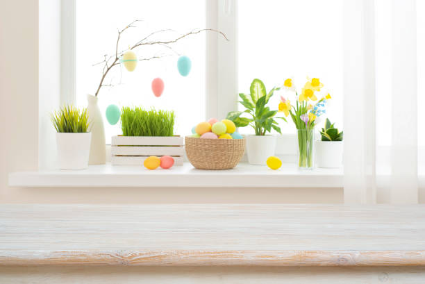 istock Empty easter table background in front of blurred multicolor flowers and eggs on sunny kitchen window sill 1997772402