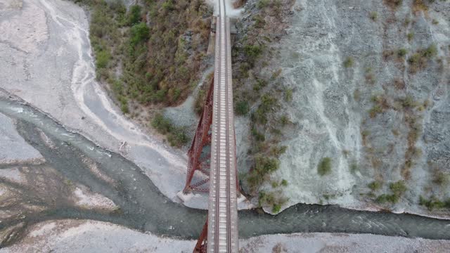 Camera moving along and old rusted metal railway bridge over a dry river bed top down view onto the railway track