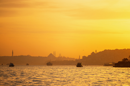 Scenic view at sunset featuring the iconic Istanbul skyline with silhouettes of famous mosques and boats on the Bosphorus.