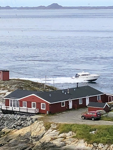 Red wooden seaside building in building, motorboat passing by. The photo was taken in Nuuk, Greenland on August 13, 2023
