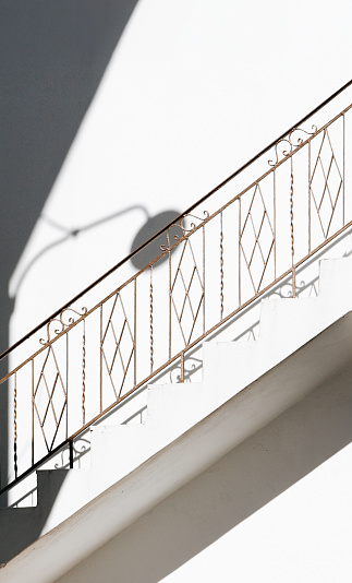 Shadow of a lamp on the wall in daylight. Stairs with railings. Naxos, Cyclades, Greece